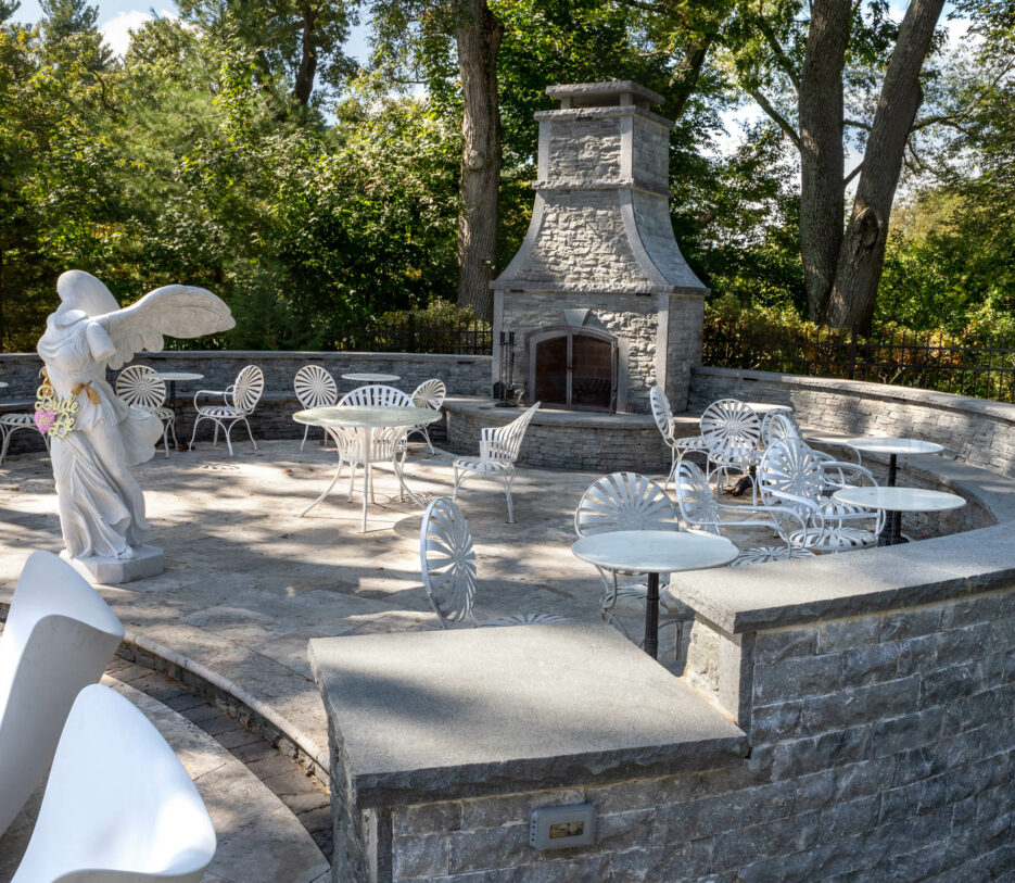 Patio area with many small tables and a marble statue and a stone fireplace.