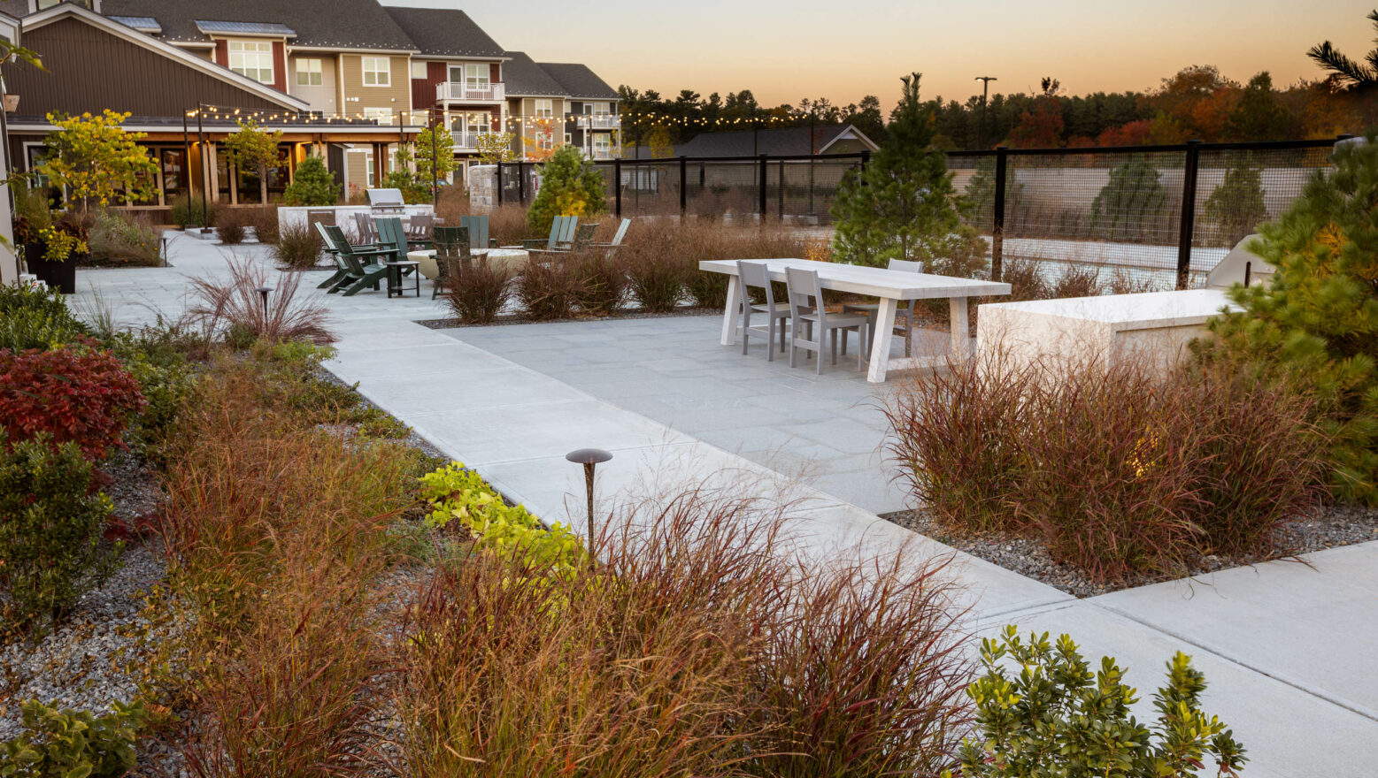 Apartment courtyard with a community tables, outdoor kitchens and lights. Commercial landscape design-build by Dex by Terra.