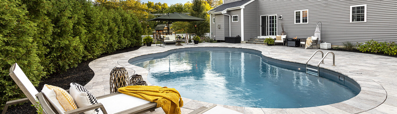 Pool chairs overlooking pool and home. Hardscape design project by Dex by Terra in Shewsbury, MA.