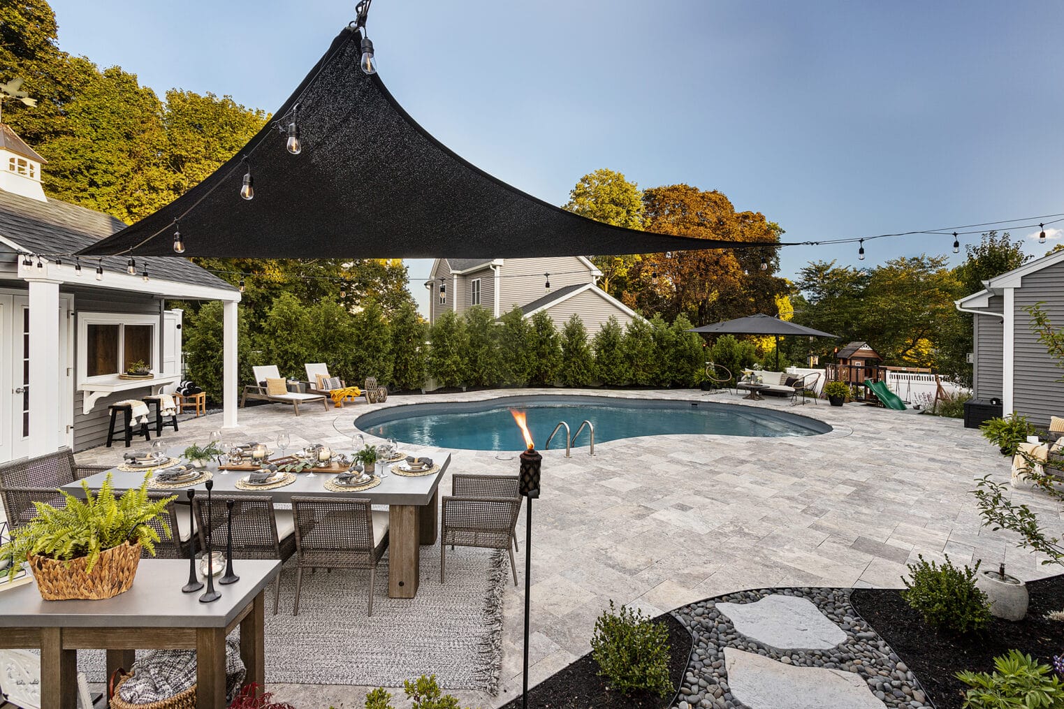 Dining table with travertine pool deck at Dex by Terra's residential hardscape design-build project in Shrewsbury, MA.