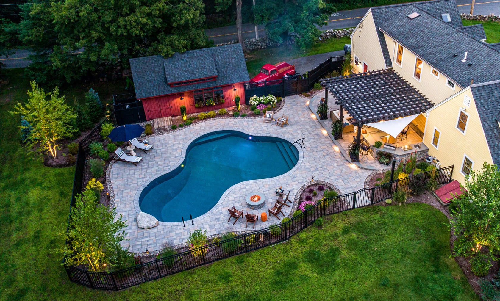 Drone view of pool deck, fire pit, and outdoor kitchen at Dex by Terra's residential landscape design project in Stow, MA.