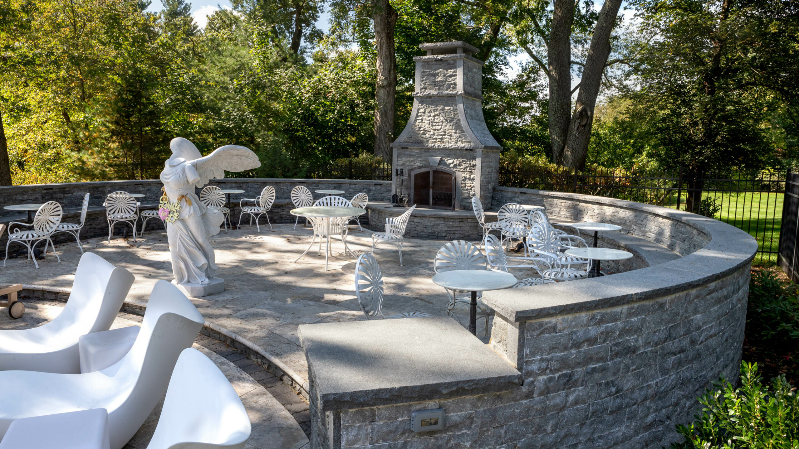 Patio area with many small tables and a marble statue and a stone fireplace.
