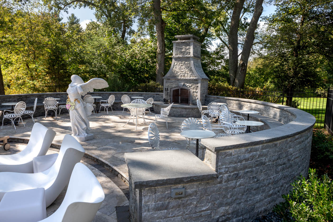 Patio area with many small tables and a marble statue and a stone fireplace.