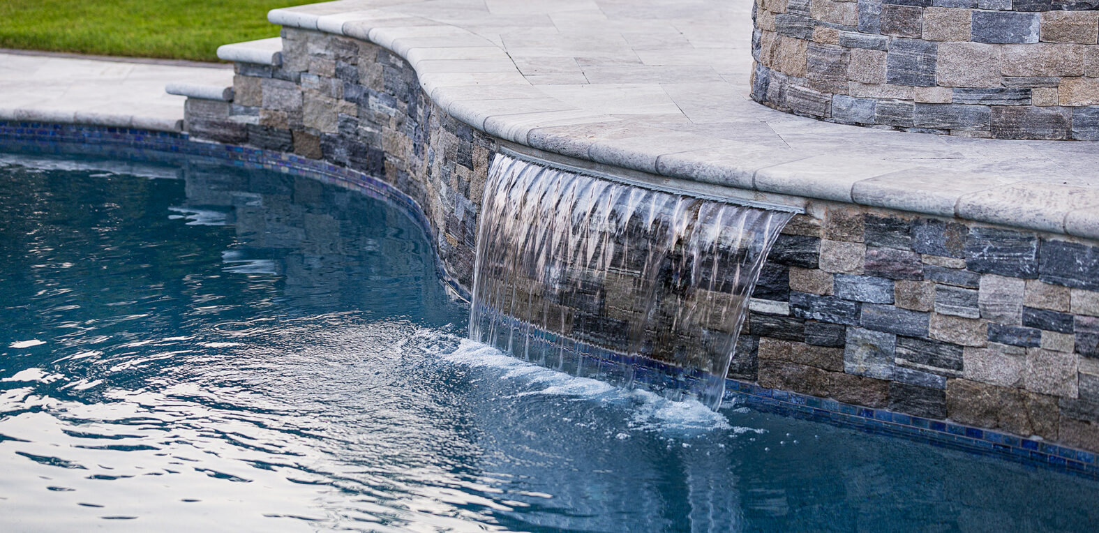 Water feature built into pool deck and flowing into pool. Dex by Terra landscape design-build in Norfolk, MA.