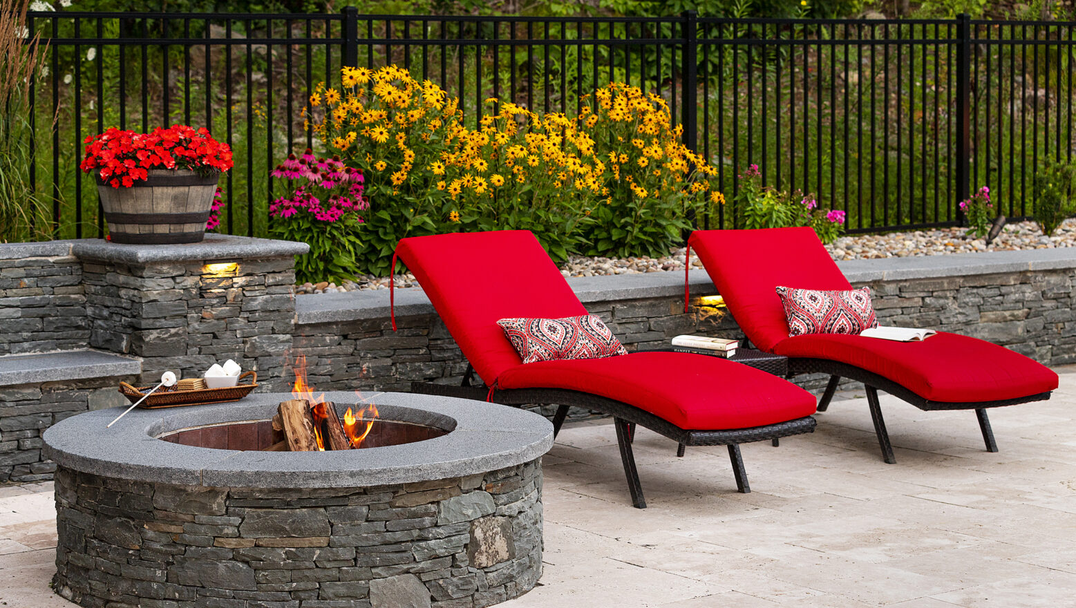 Pool chairs by the stone fire pit and seating wall with s'mores. Dex by Terra Hardscaping & Landscaping project in Sterling Massachusetts.