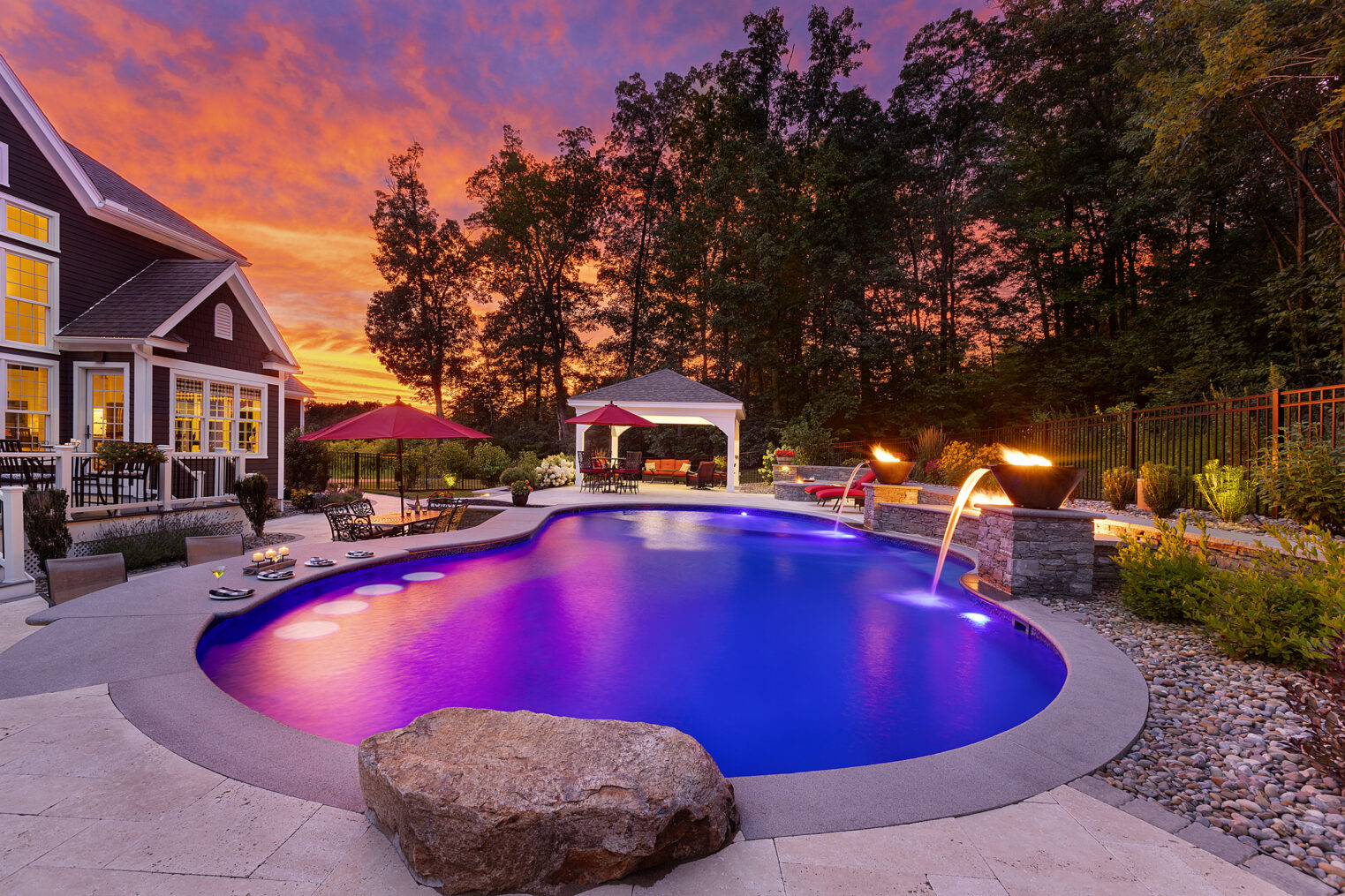 Sunset by the pool in Sterling, MA. Pool deck with water/fire features and a jump rock. Built by Dex by Terra.
