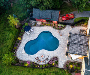 Drone view of hardscape project with pool, fire pit, & outdoor kitchen. Landscape design-build by Dex by Terra in Stow, MA.