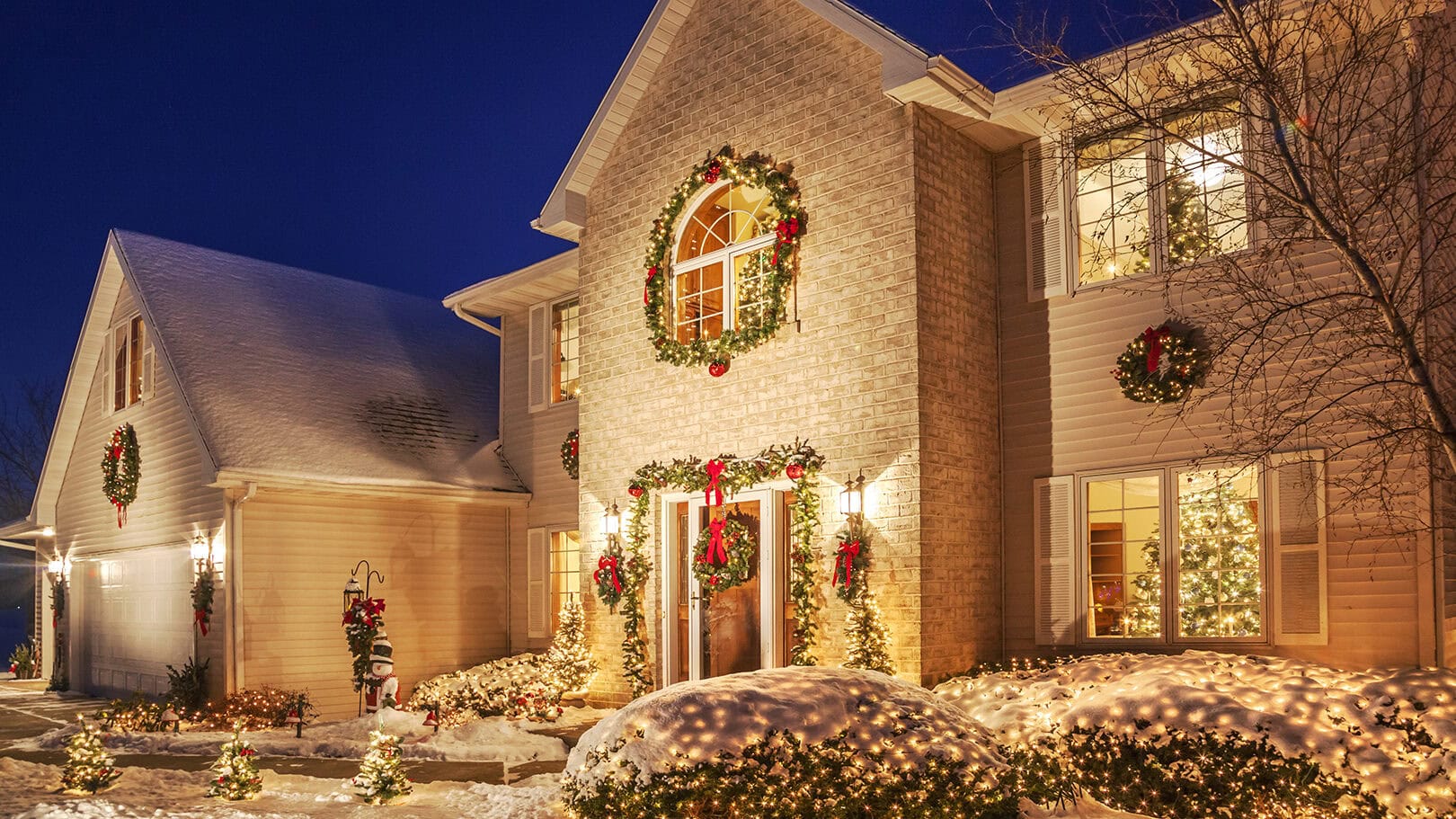 Holiday decorated home at evening with Christmas lighting, and fluffy snow.