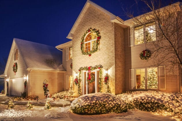 Holiday decorated home at evening with Christmas lighting, and fluffy snow.