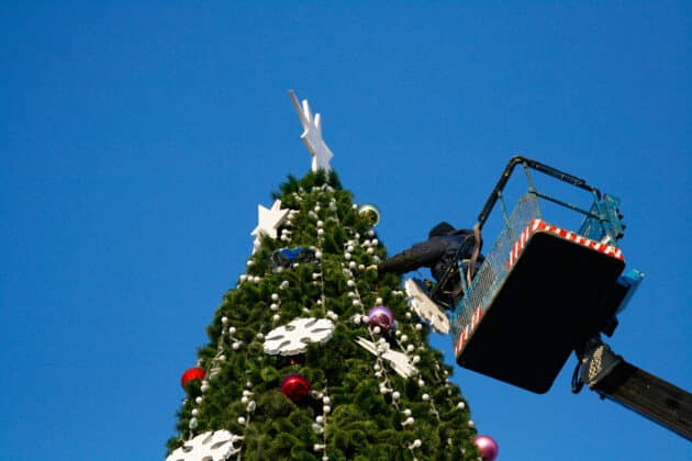 A worker decorates a large Christmas tree using a lift.