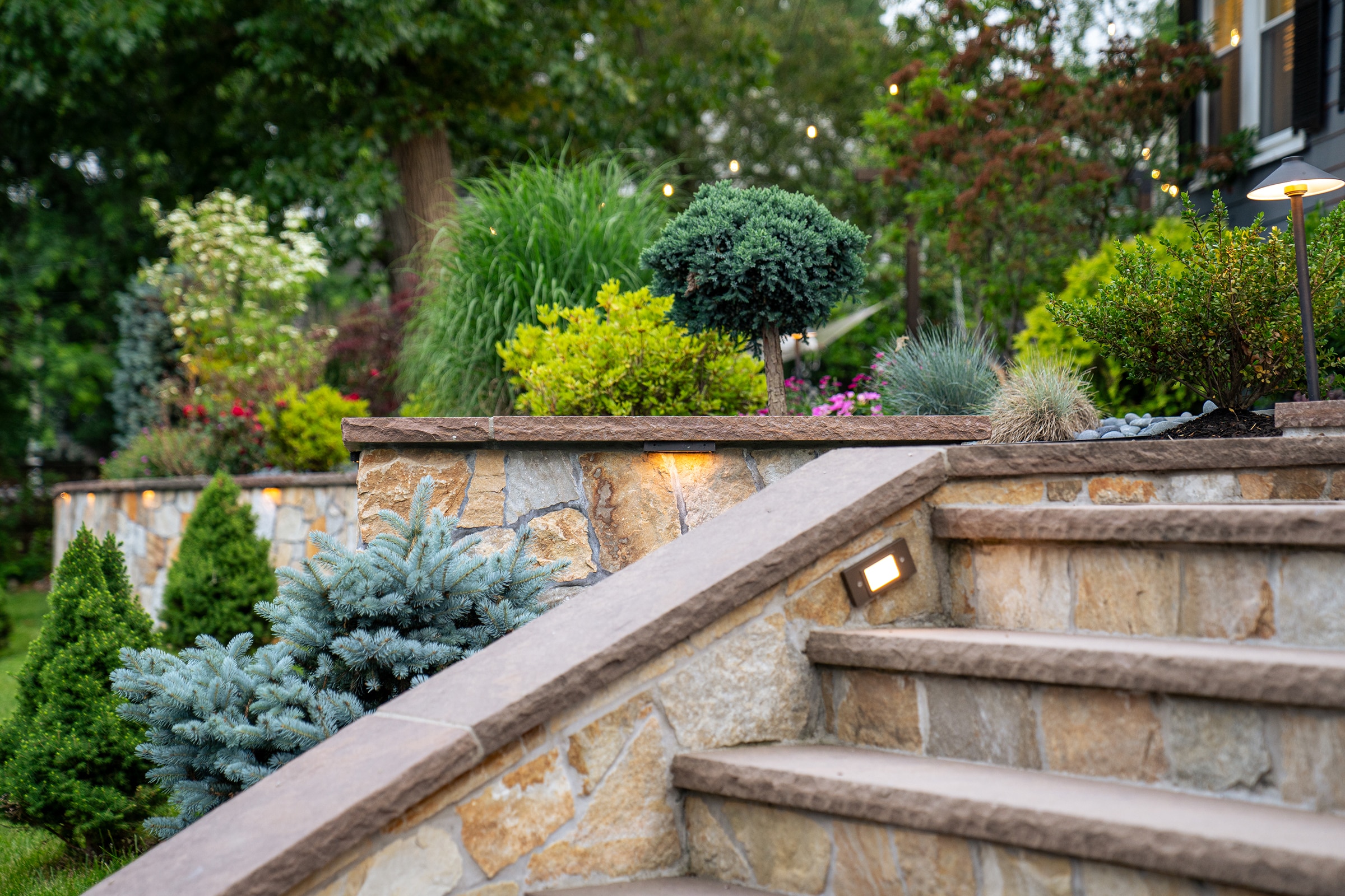 Stone steps, and a stone retaining wall with built-in low voltage landscape lighting in Needham, MA.