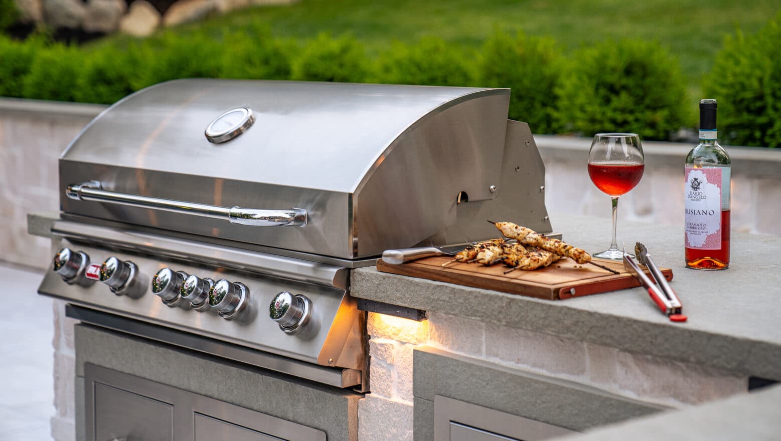An outdoor kitchen with stainless steel grill and freshly prepared grilled chicken with red wine.