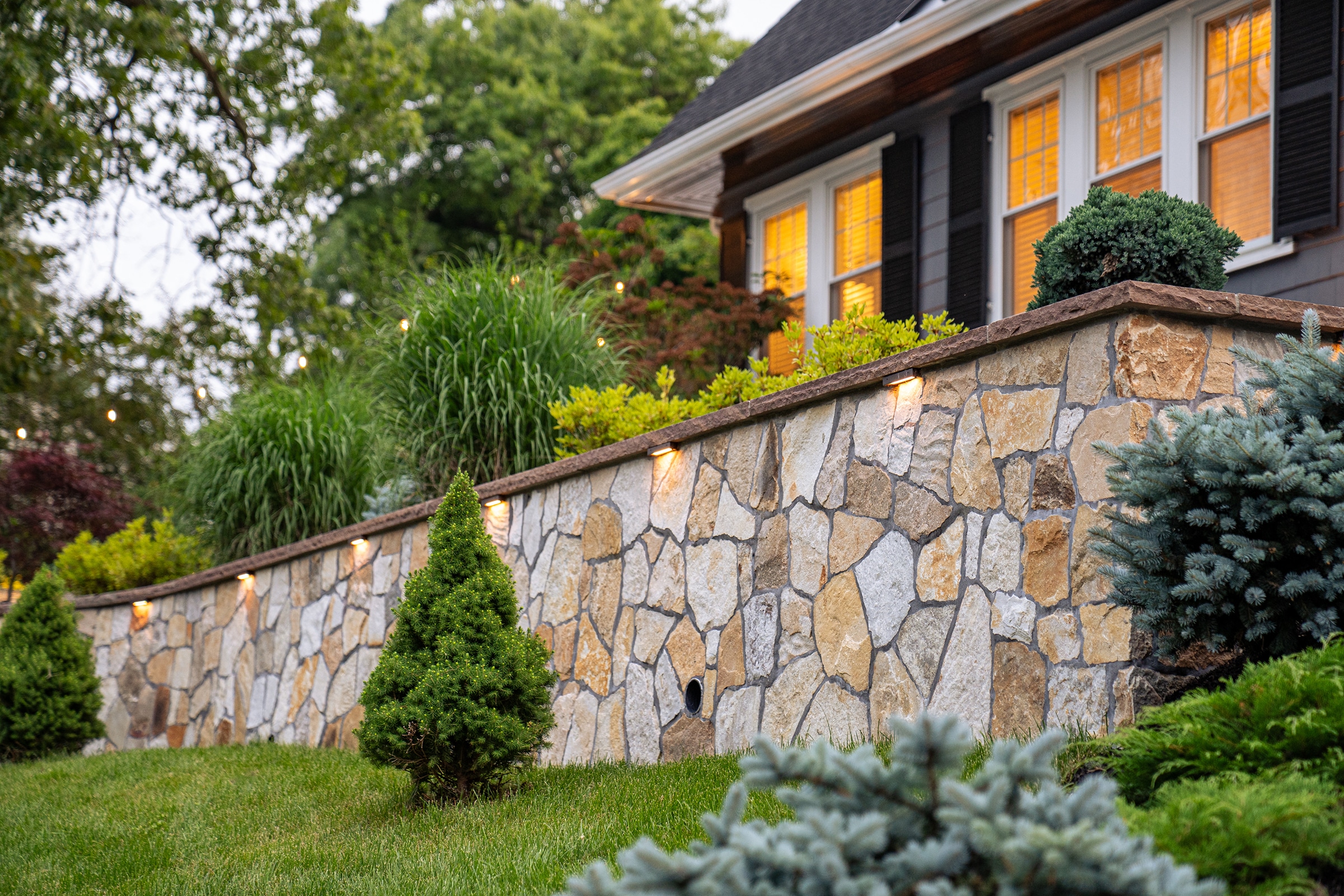 A stone retaining wall with built-in low voltage landscape lighting in Needham, MA.