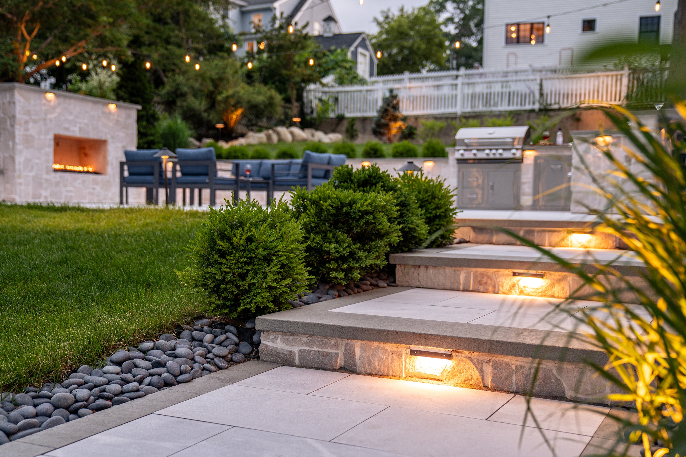 Stone walkway with stone steps and buit-in low voltage lighting. Backyard patio and outdoor kitchen in the background.