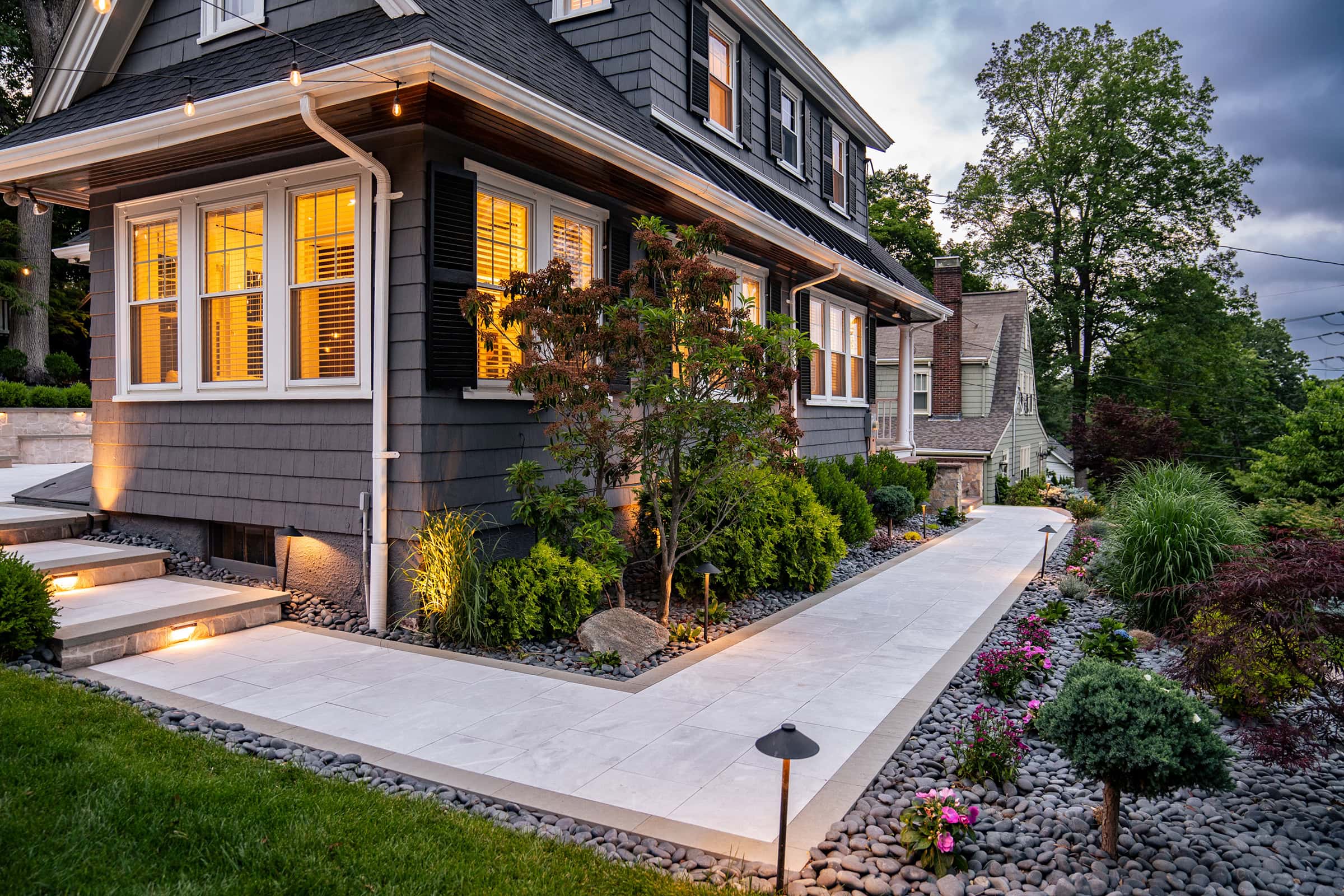 A Needham, MA, home with stone paver front walkway, landscaping, and landscape lighting designed and built by Dex by Terra,