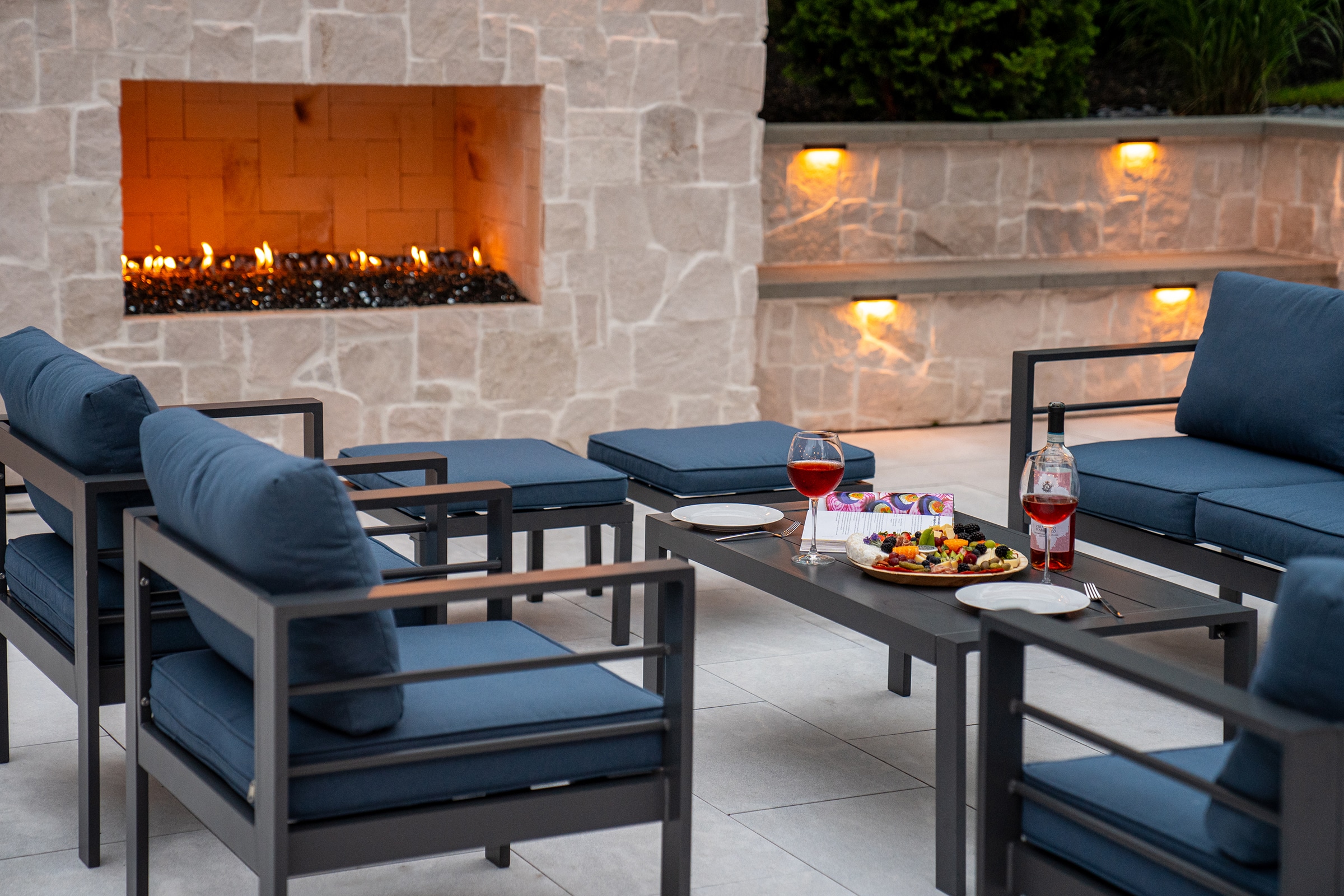 Patio furniture with charcuterie board and wine glasses by the outdoor gas fireplace in Needham, MA.