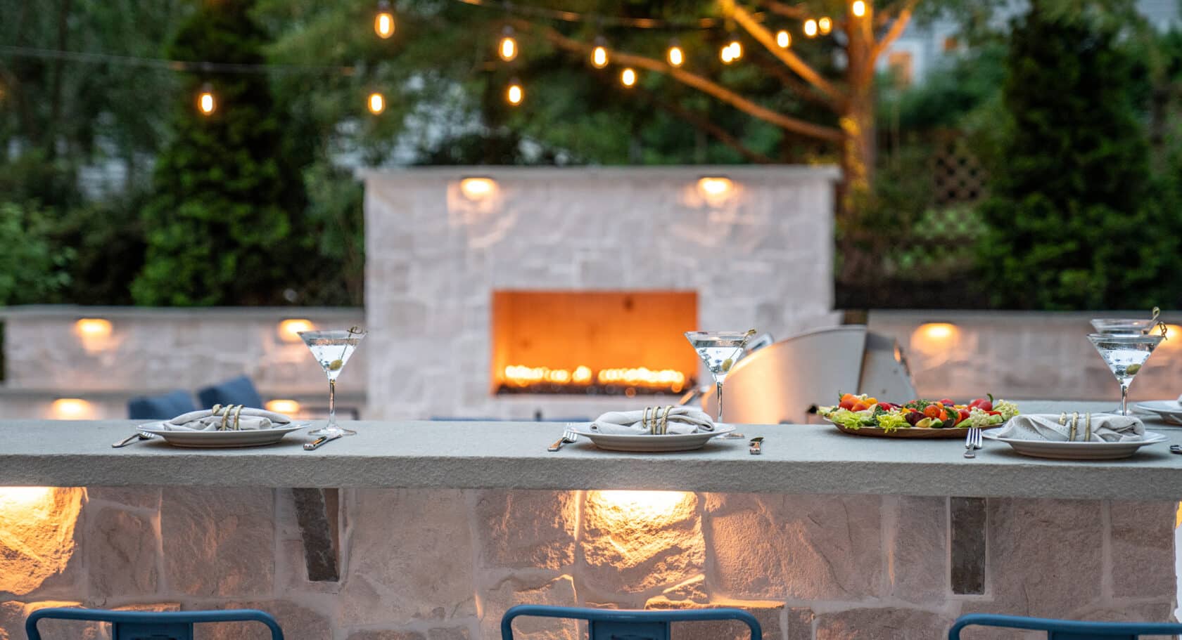 Evening martinis at the patio bar overlooking a gas fireplace with outdoor string lights & integrated landscape lighting.