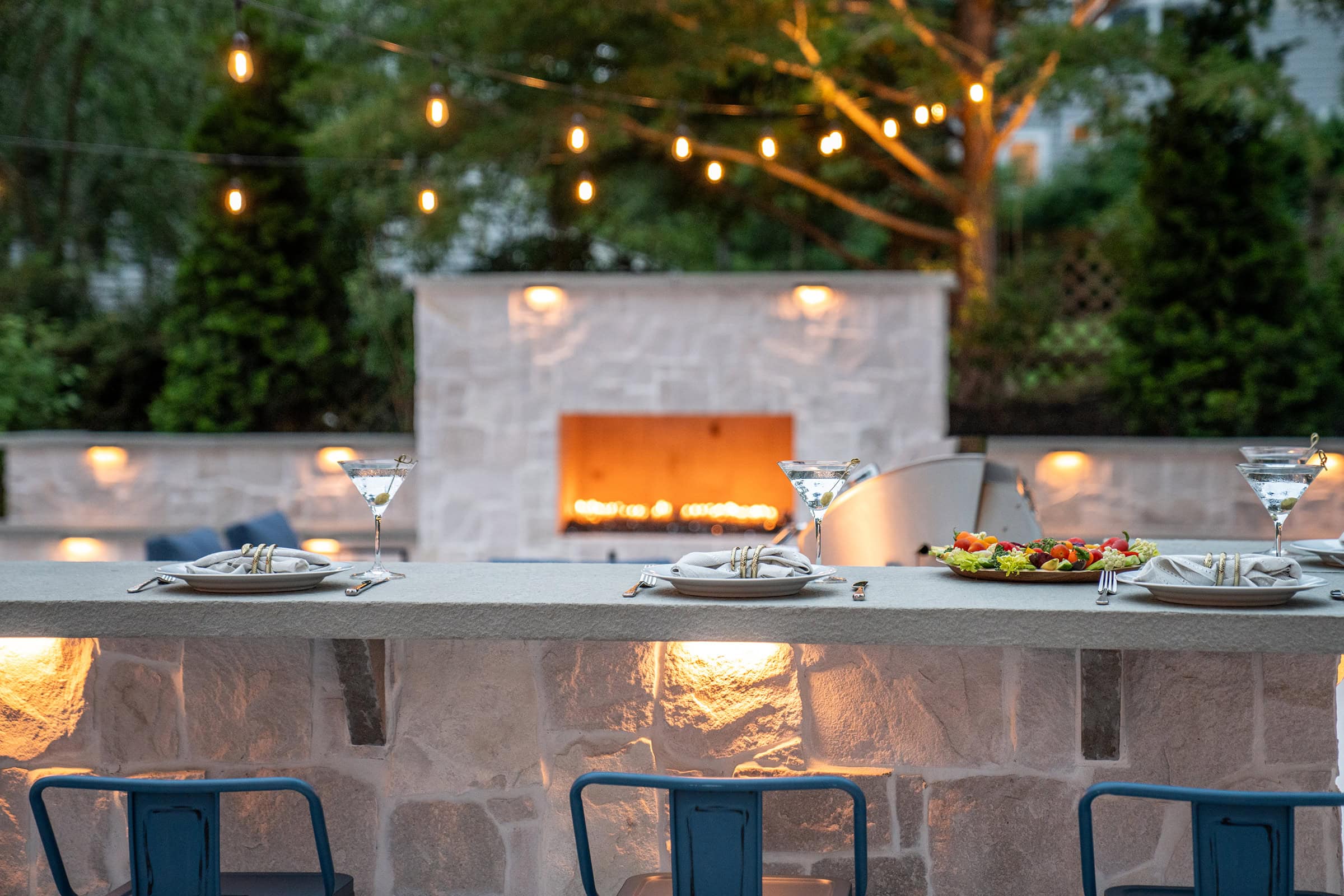 Evening martinis at the patio bar overlooking a gas fireplace with outdoor string lights & integrated landscape lighting.