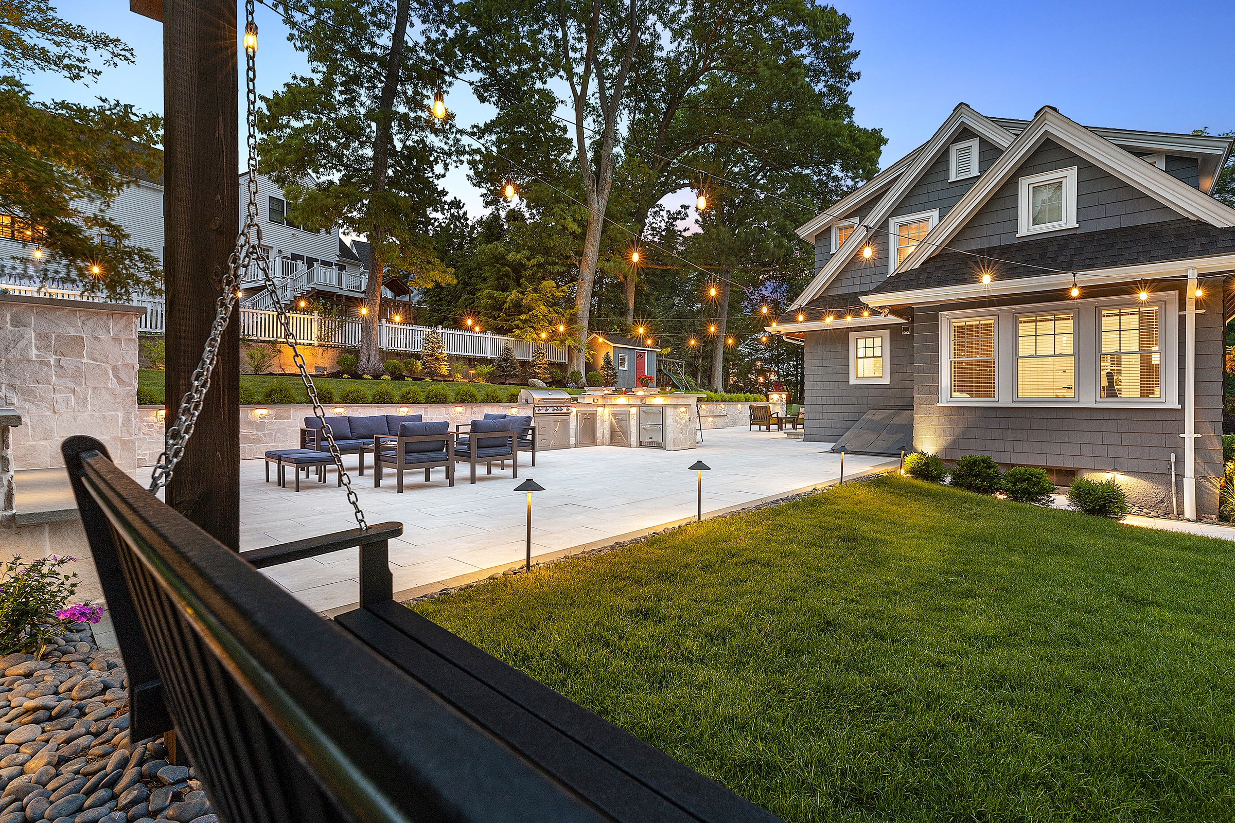 Backyard patio in Needham, Massachusetts with patio furniture, outdoor kitchen, and outdoor lighting.