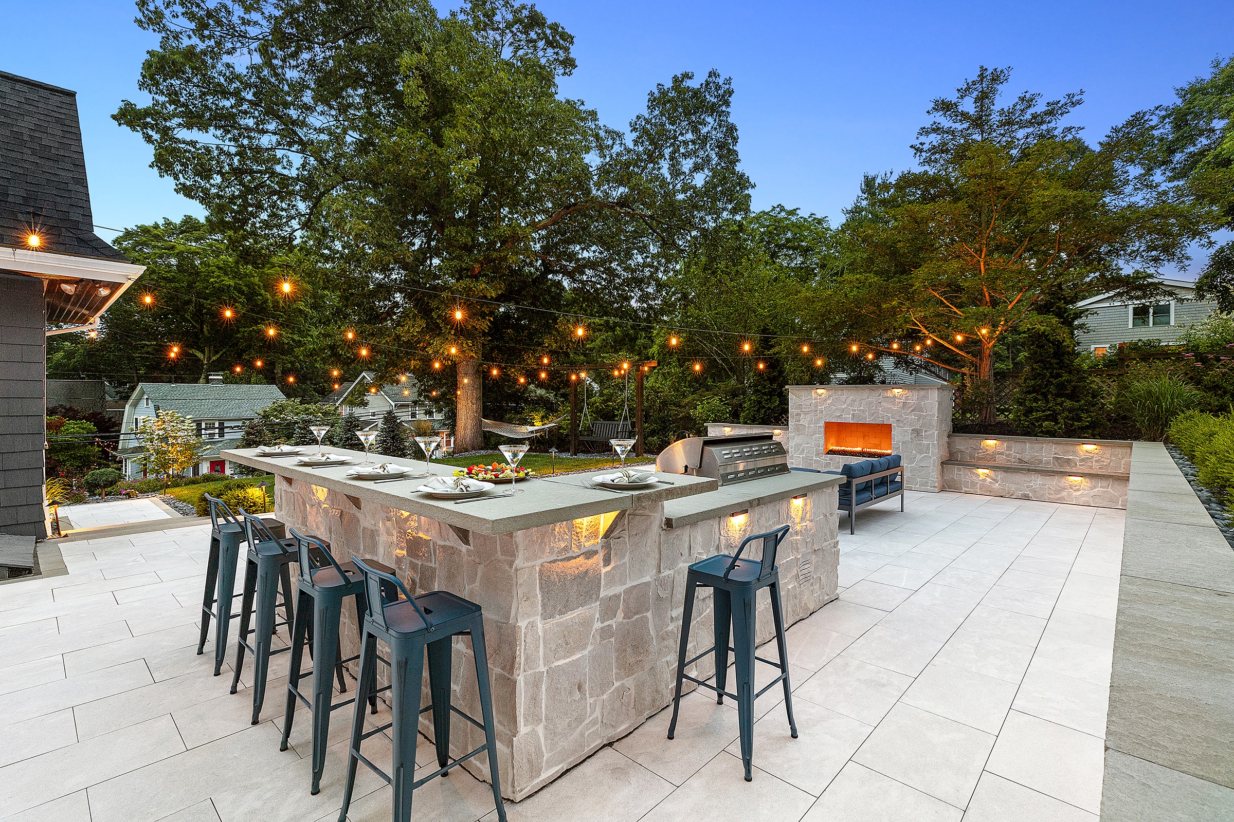 Place settings and barstools are at the ready by the outdoor bar and outdoor kitchen on the Needham, MA backyard patio.