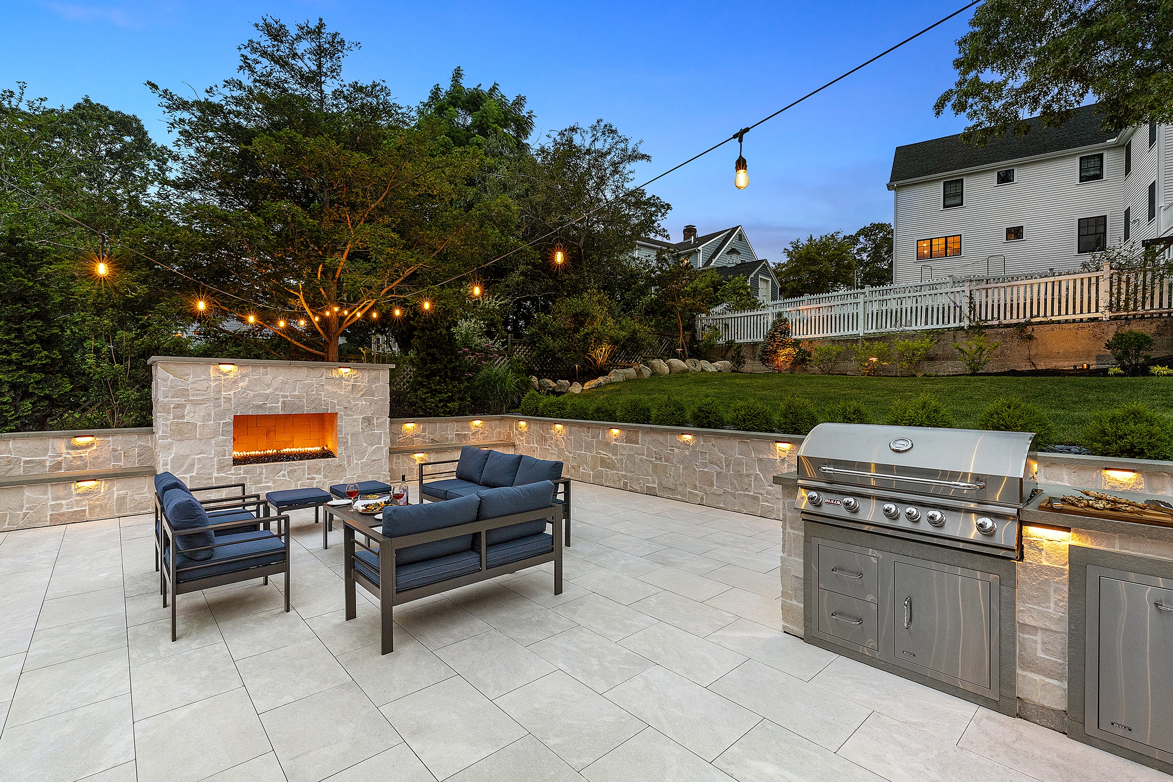 Outdoor fireplace, patio furniture, and a stainless steel gas grill on a natural stone paver patio.