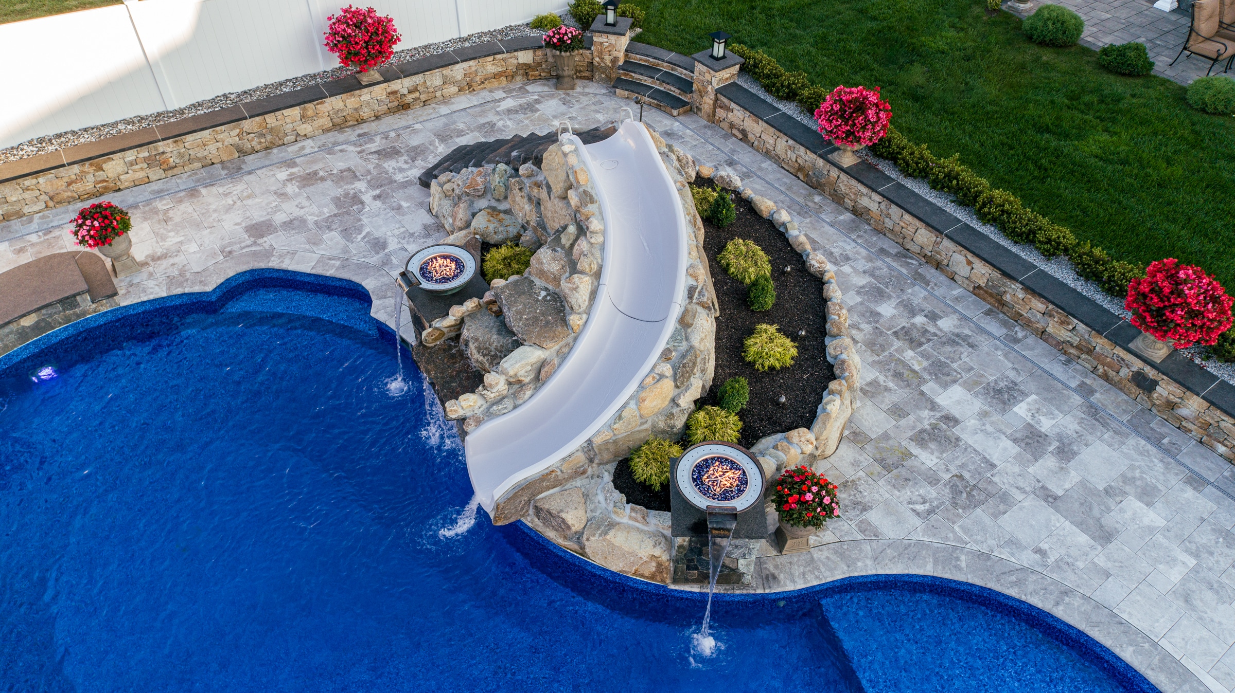 A custom Dex by Terra waterslide with a landscaping bed and water/fire features built with natural stone boulders.