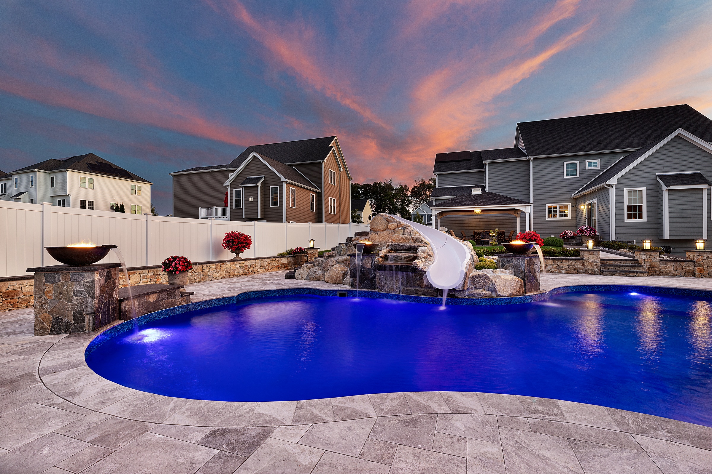 A backyard in Grafton, Massachusetts with a pool deck, waterslide, and fire and water features all built by Dex by Terra.