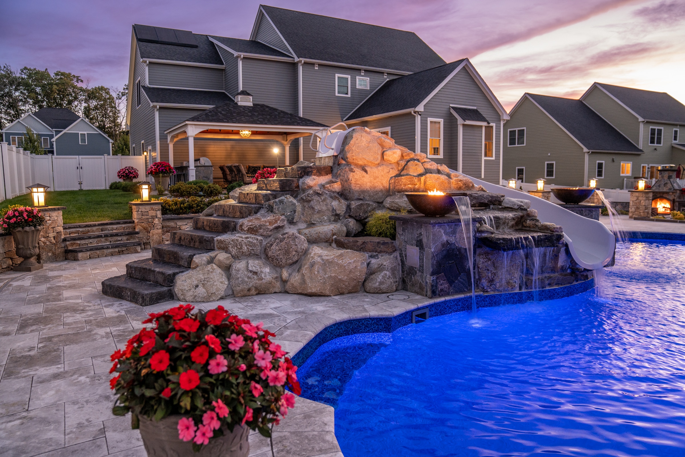A sunset illuminates the evening sky over this pool deck and waterslide built by Dex by Terra in Grafton, Massachusetts.
