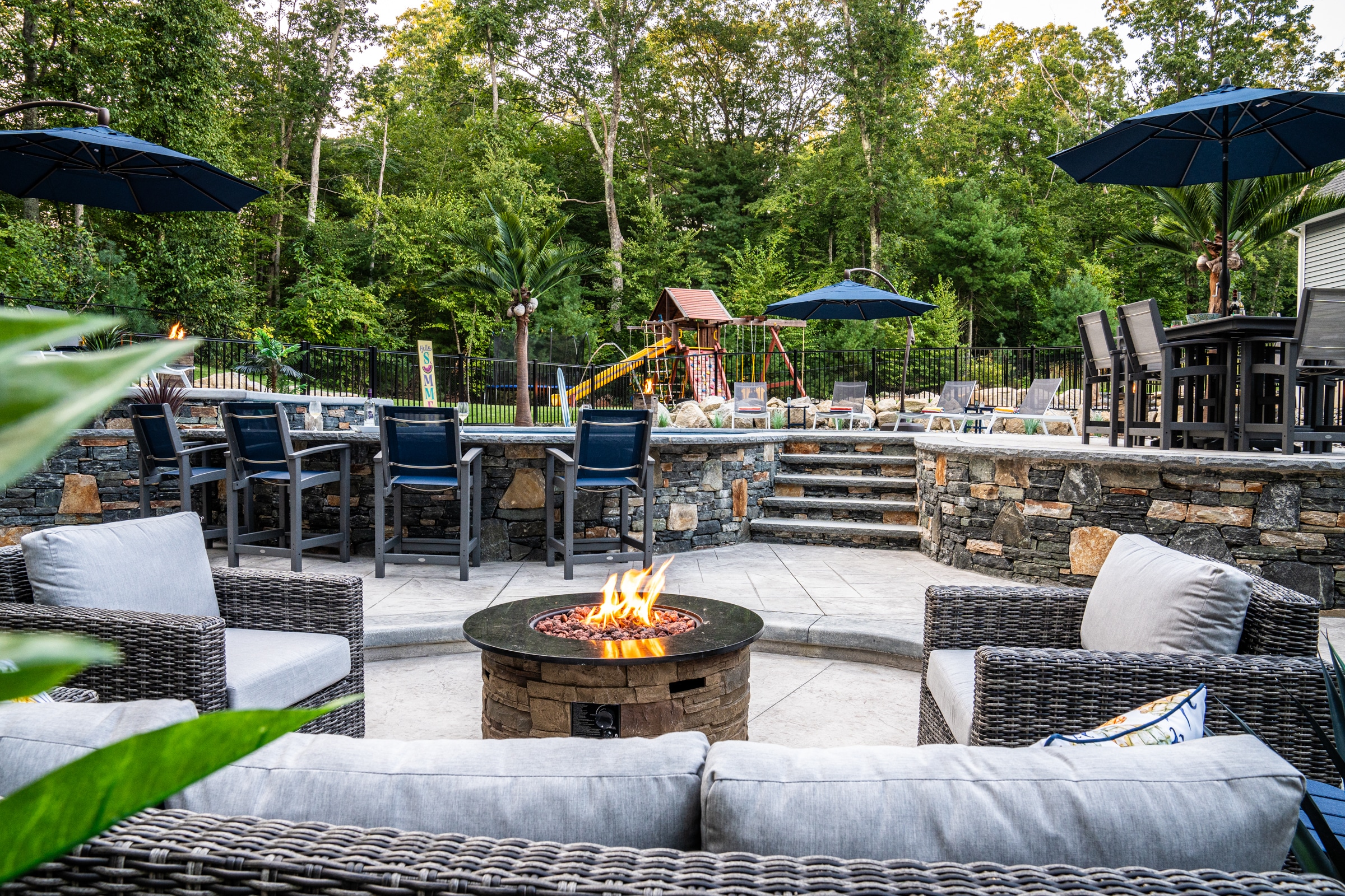 A stamped concrete fire pit patio with an elevated pool deck and poolside bar in the background. Dex by Terra hardscape project.