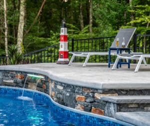 Bask in the sun on this stamped concrete and stone veneer sundeck with an integrated water feature. A Dex by Terra hardscape.