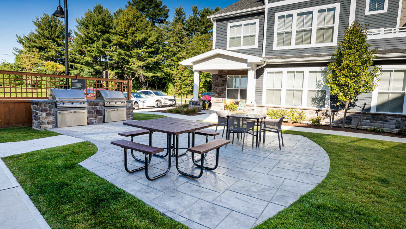 Amenity area with stamped concrete patio, outdoor kitchens, and tables. Commercial hardscape project by Dex by Terra.