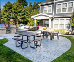 Amenity area with stamped concrete patio, outdoor kitchens, and tables. Commercial hardscape project by Dex by Terra.