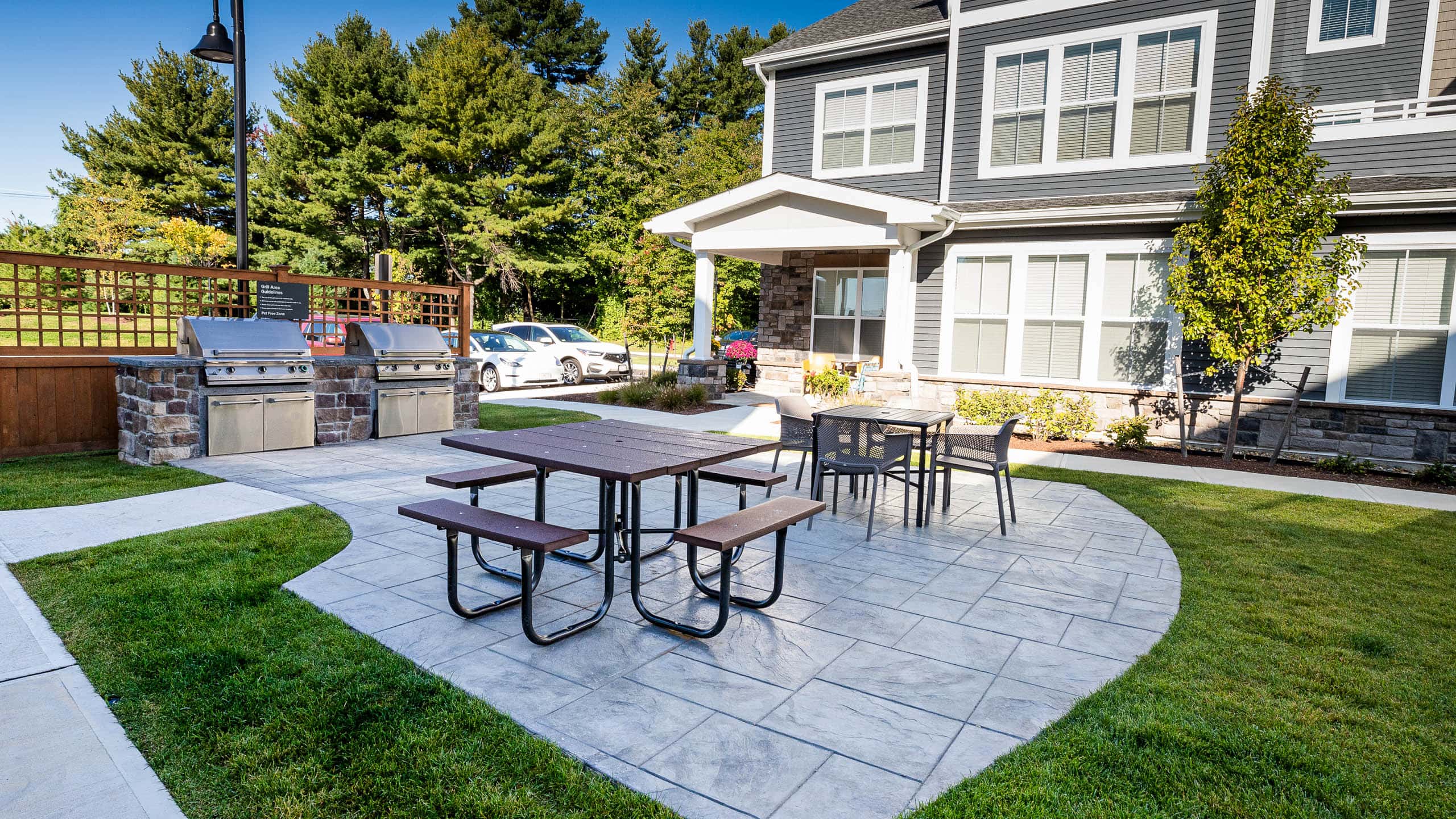 Amenity area with stamped concrete patio, outdoor kitchens, and tables. Commercial hardscape project by Dex by Terra.