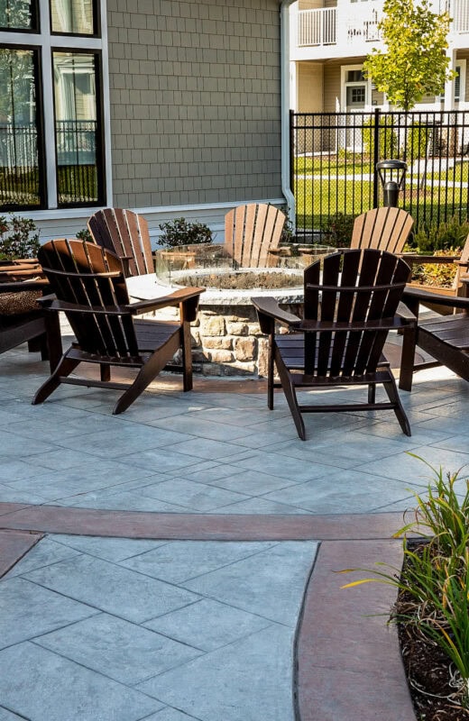 Chairs around a fire pit with stamped and colored concrete patio. Dex by Terra commercial hardscape in MA.