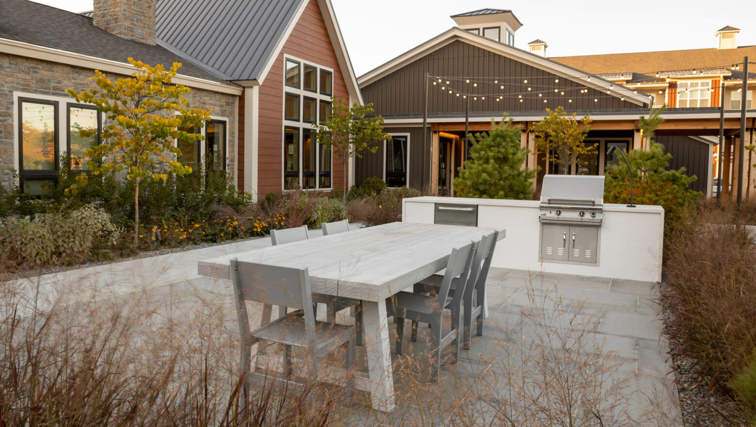 Dining area with table, chairs, and outdoor kitchen at a luxury apartment complex. Dex by Terra Hardscape project in MA.