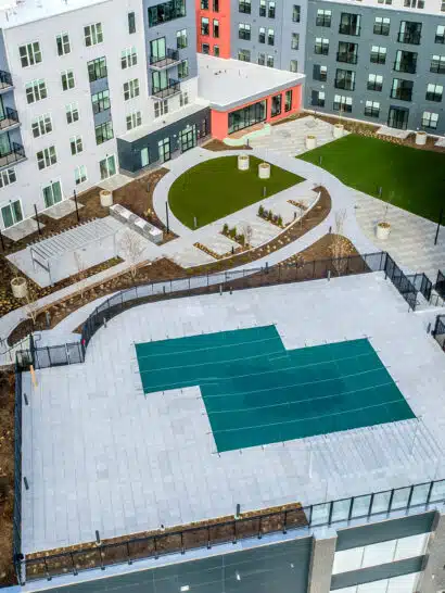 The Revington podium-level courtyard in Worcester, MA with pool deck, patios, outdoor kitchens, walkways, & synthetic turf.