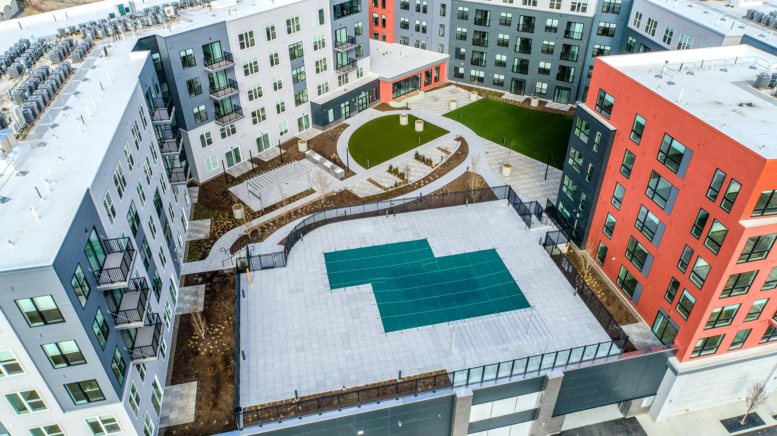 The Revington podium-level courtyard in Worcester, MA with pool deck, patios, outdoor kitchens, walkways, & synthetic turf.
